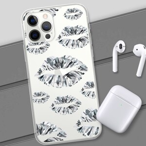 May include: A clear phone case with a white background and a repeating pattern of black and white diamond-shaped lips. The case is shown on a grey surface with a pair of white wireless earbuds and a white charging case.