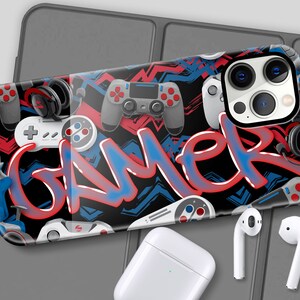 May include: A black phone case with a gamer theme. The case features a red, blue, and white graffiti design with the word "GAMER" in large letters. The case also features images of video game controllers and headphones.