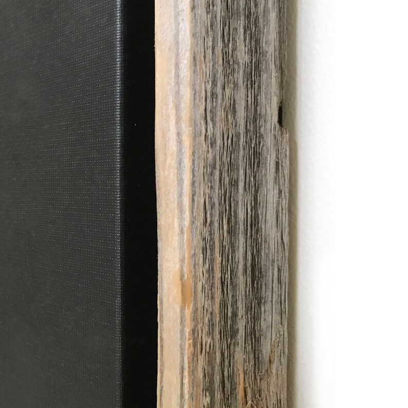 May include: Close-up of the edge of a black canvas painting framed in a rustic wood frame. The wood has a natural, weathered finish with knots and grain patterns.