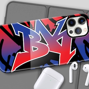 May include: A phone case with a red, blue, and black graffiti design. The case has a camera lens cutout and a clear back.