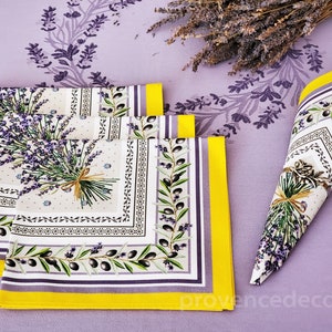May include: Set of four lavender and olive branch patterned napkins with yellow trim. The napkins are folded and arranged on a purple background with a bunch of dried lavender.
