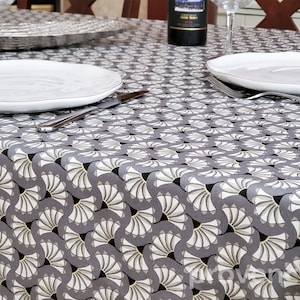 May include: A gray tablecloth with a white and gold geometric pattern of fans. Two white dinner plates are set on the table with silverware.