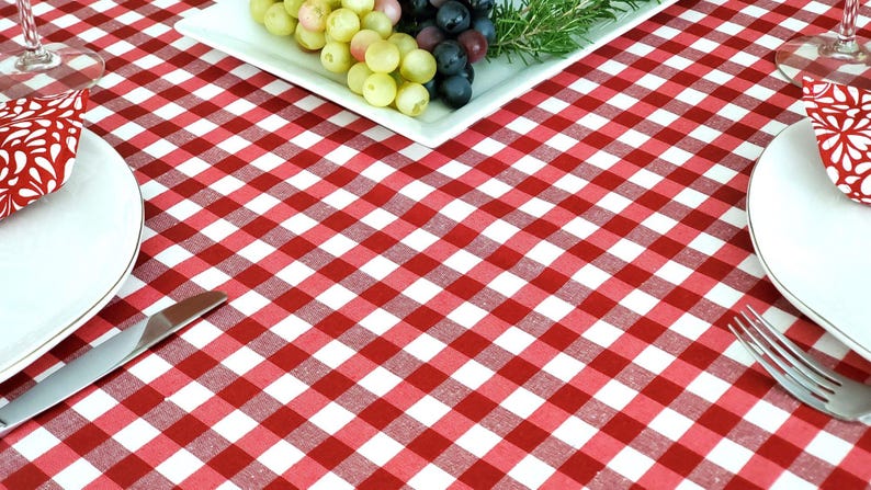 Pu&ograve; includere: Tovaglia a quadri rossi e bianchi con due posti a tavola, ognuno con un piatto bianco, un tovagliolo e una forchetta. Un piatto bianco con uva verde e viola &egrave; al centro della tovaglia.