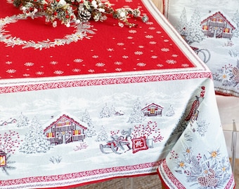 Puede incluir: Mantel de mesa rojo y blanco con una escena de invierno que presenta un pueblo nevado, pinos y un trineo. El mantel tiene un borde rojo con un patrón de copo de nieve blanco.