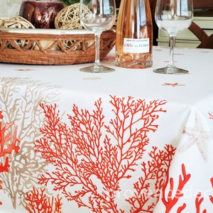 May include: White tablecloth with a coral reef design in shades of red and tan. The tablecloth is decorated with starfish and is set with wine glasses and a bottle of rosé wine.