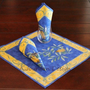 May include: A blue and yellow square placemat with a floral design and a folded napkin on top. The placemat has a yellow border with a decorative pattern.