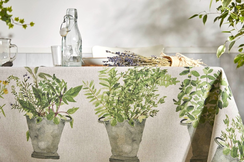 May include: A beige linen tablecloth with a green botanical print featuring various herbs and plants in galvanised metal pots. The tablecloth has a rustic and farmhouse style.