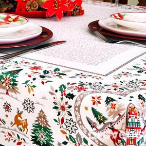 May include: White tablecloth with a festive Christmas design featuring red and green trees, houses, and snowflakes. Two white plates with red trim are set on the table.