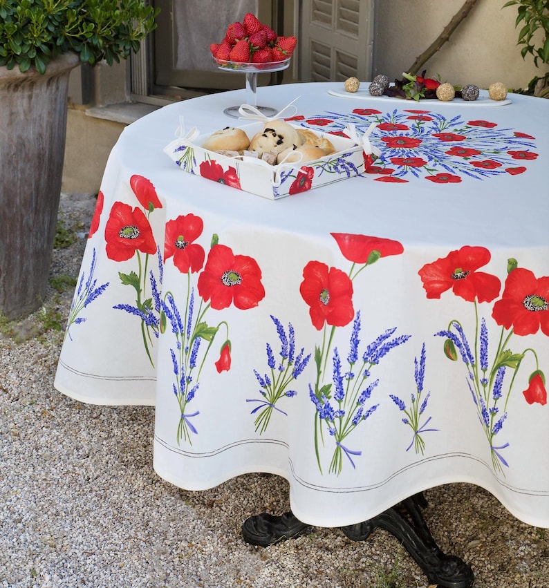May include: White round tablecloth with a red poppy and lavender floral pattern. The tablecloth is on a round table with a basket of pastries and a bowl of strawberries.