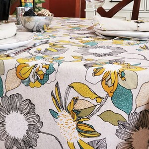 May include: A white tablecloth with a floral pattern in shades of yellow, green, and gray. The tablecloth is laid on a table with two place settings.