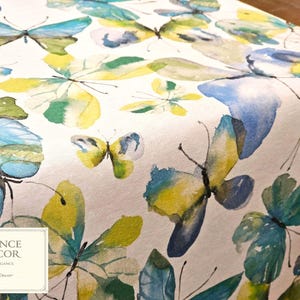 May include: White table runner with a watercolor butterfly pattern in shades of blue, yellow, and green. The butterflies are of varying sizes and are scattered across the fabric. The Provence Decor logo is in the lower left corner.