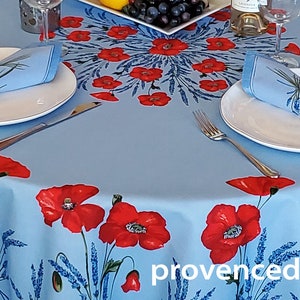 May include: A blue round tablecloth with a poppy and lavender floral pattern. Two place settings are set with white plates, silverware, and blue napkins with a lavender design. The tablecloth has the text "provencedecor" printed on it.