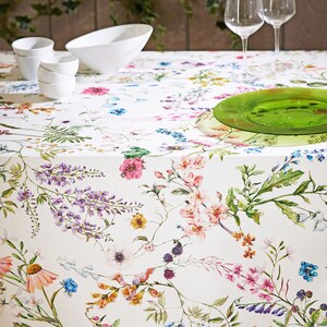 May include: White tablecloth with a floral pattern featuring pink, purple, yellow, and blue flowers. The tablecloth is set with white bowls and two wine glasses.