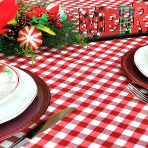 Pu&ograve; includere: Una tovaglia a quadri rossi e bianchi con un cartello di legno che dice "Merry". Ci sono due posti a tavola con piatti bianchi e sottopiatti rossi. Un centrotavola natalizio con una stella di Natale, verde e bastoncini di zucchero &egrave; sullo sfondo.