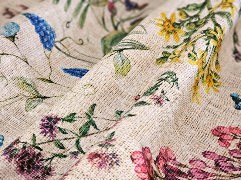 May include: A beige fabric with a floral pattern featuring blue, yellow, pink, and green flowers. The fabric has a textured woven look.