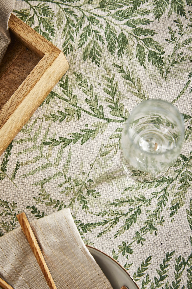 May include: A close-up of a table setting with a green fern pattern tablecloth, a wooden tray, a glass, a napkin, and wooden chopsticks.