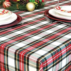 May include: A white tablecloth with a red, green, and black plaid pattern. Two place settings are visible, each with a white plate, a red charger plate, and a silver fork.