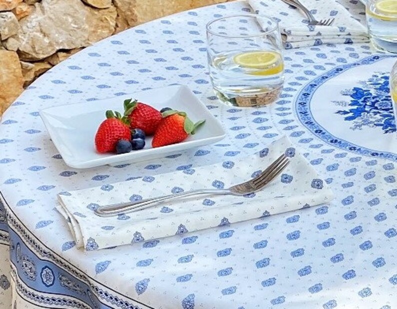 May include: A white tablecloth with a blue and white paisley pattern. A white plate with strawberries and blueberries is on the tablecloth. A white napkin with a blue and white paisley pattern is folded on the tablecloth. A glass of water with a lemon slice is on the tablecloth.