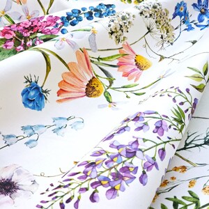 May include: White fabric with a floral print featuring a variety of flowers in shades of pink, blue, purple, yellow, and orange. The flowers are arranged in a random pattern and are surrounded by green leaves.