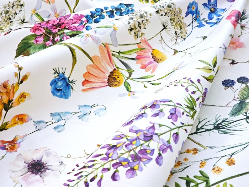 May include: White fabric with a floral print featuring a variety of flowers in shades of pink, blue, purple, yellow, and orange. The flowers are arranged in a random pattern and are surrounded by green leaves.