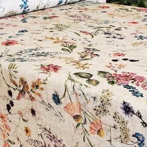 May include: A beige fabric with a floral pattern featuring various shades of pink, blue, yellow, and green flowers. The fabric has a subtle linen texture.