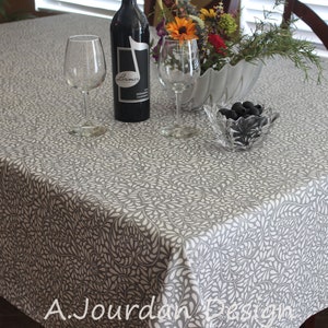 May include: A gray and white patterned tablecloth with a leaf design, set for a meal. The table is set with wine glasses, a bottle of wine, a bowl of olives, and a floral centerpiece. The text "A. Jourdan Design" is visible.