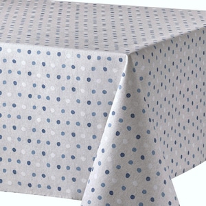 May include: A light beige tablecloth with a repeating pattern of blue and white polka dots. The tablecloth is made of a soft fabric and is folded over a table, showcasing the pattern and texture.