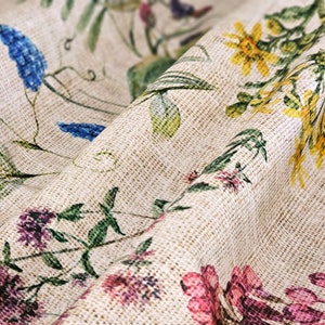 May include: A beige fabric with a floral pattern featuring blue, yellow, pink, and green flowers. The fabric has a textured woven look.