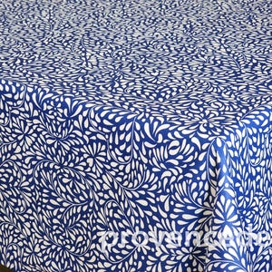 May include: A blue and white tablecloth with a repeating pattern of white teardrop shapes against a deep blue background. The fabric is folded over a table, showing the pattern's continuity.