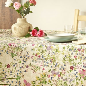 May include: A beige tablecloth with a floral pattern featuring pink, purple, and blue flowers. The tablecloth is set with a bowl, plates, and glasses.