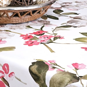 May include: White tablecloth with a watercolor floral pattern featuring pink and red flowers, green leaves, and gray accents. A woven basket with a silver rim is in the upper left corner.