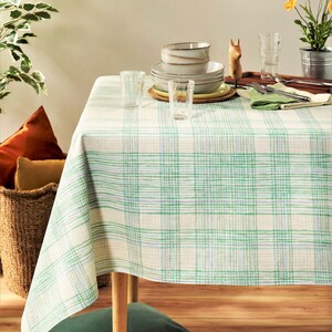 May include: A white tablecloth with a green and white plaid pattern. The tablecloth is set with dishes, glasses, and silverware.
