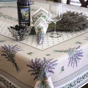 May include: A rectangular tablecloth featuring a beige background with a repeating pattern of purple lavender sprigs and green olive branches. The border includes a decorative geometric trim, while the center displays a white dotted panel.