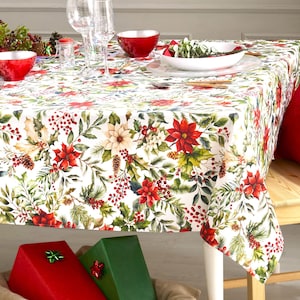 May include: White tablecloth with a red and green floral pattern featuring poinsettias, holly, berries, and pine cones. The tablecloth is set for a holiday dinner with plates, silverware, and glasses.