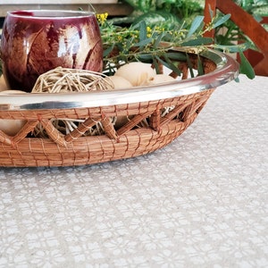 May include: A woven wicker basket with a silver rim, filled with decorative balls and a red glass candle holder.