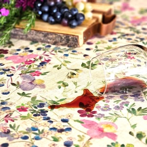 May include: A glass of red wine has been spilled on a white tablecloth with a floral pattern. The wine has created a dark red stain on the tablecloth.