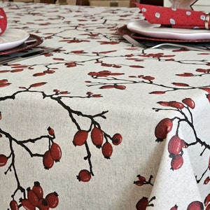 May include: A white tablecloth with a red and black floral pattern. The tablecloth features a repeating design of branches with red berries.