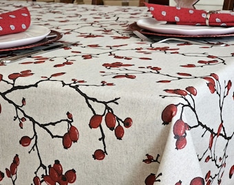 Puede incluir: Un mantel blanco con un patrón floral rojo y negro. El mantel presenta un diseño repetitivo de ramas con bayas rojas.