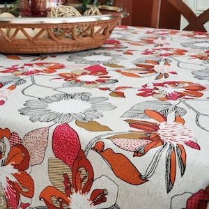 May include: A white tablecloth with a floral pattern featuring orange, red, and gray flowers. The tablecloth has a textured linen-like appearance.