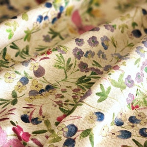 May include: A close-up of a white fabric with a floral pattern. The fabric features a variety of small flowers in shades of blue, purple, pink, and yellow. The flowers are scattered randomly across the fabric, creating a delicate and whimsical design.