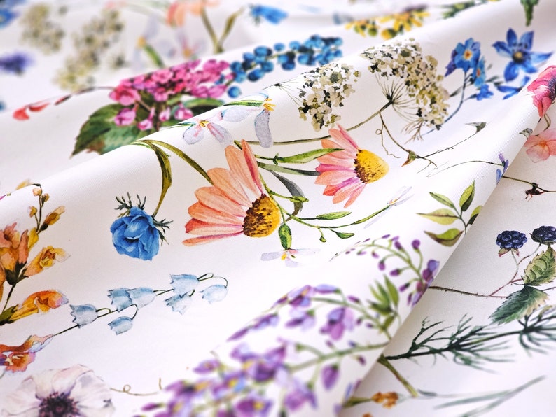 May include: White fabric with a floral print featuring various flowers in shades of pink, blue, purple, and yellow. The fabric has a subtle texture and a soft, flowing drape.