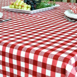 May include: A red and white checkered tablecloth covers a table set for a meal. White plates, silverware, and napkins with a red floral pattern are visible. Grapes and rosemary are on a serving dish.