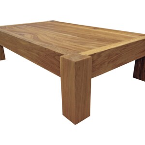 May include: A solid wood coffee table with a rectangular top and four thick legs. The table is made of natural wood with a light brown finish.