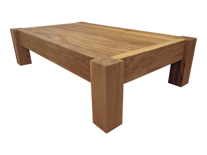 May include: A solid wood coffee table with a rectangular top and four thick legs. The table is made of natural wood with a light brown finish.
