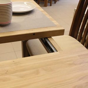 Puede incluir: Una mesa de madera con una extensión de hoja. La mesa está hecha de madera clara y tiene un acabado natural. La hoja se guarda debajo de la superficie de la mesa y se puede sacar para extender la mesa.