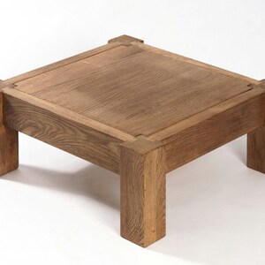 May include: A square wooden coffee table with a light brown finish. The table has a simple design with four legs and a thick top.