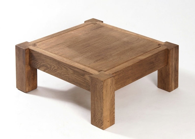 May include: A square wooden coffee table with a light brown finish. The table has a simple design with four legs and a thick top.