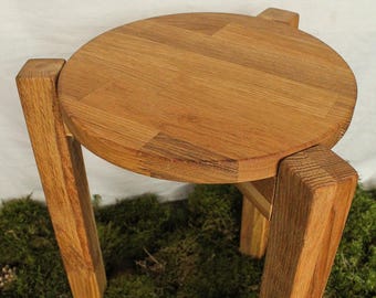 Può includere: Uno sgabello rotondo in legno con quattro gambe. Lo sgabello è realizzato in legno marrone chiaro e ha una finitura liscia e lucida.