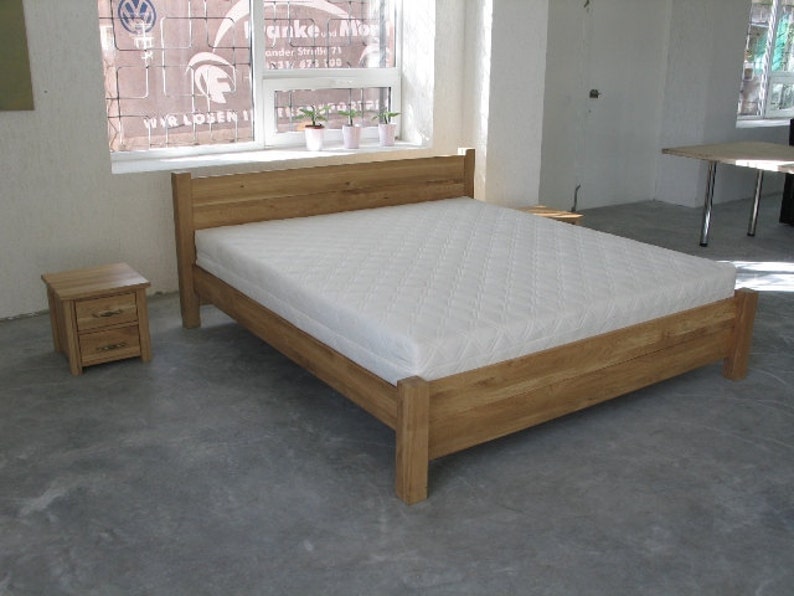 Pu&ograve; includere: Un letto con struttura in legno e un materasso bianco. La struttura del letto ha un design semplice con una testata e un piede. C'&egrave; un piccolo comodino in legno accanto al letto.