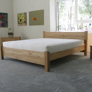 Pu&ograve; includere: Un letto con una struttura in legno e un materasso bianco. La struttura del letto &egrave; in legno naturale e ha un design semplice. Il letto si trova in una stanza con pareti bianche e una finestra con vista sugli alberi.